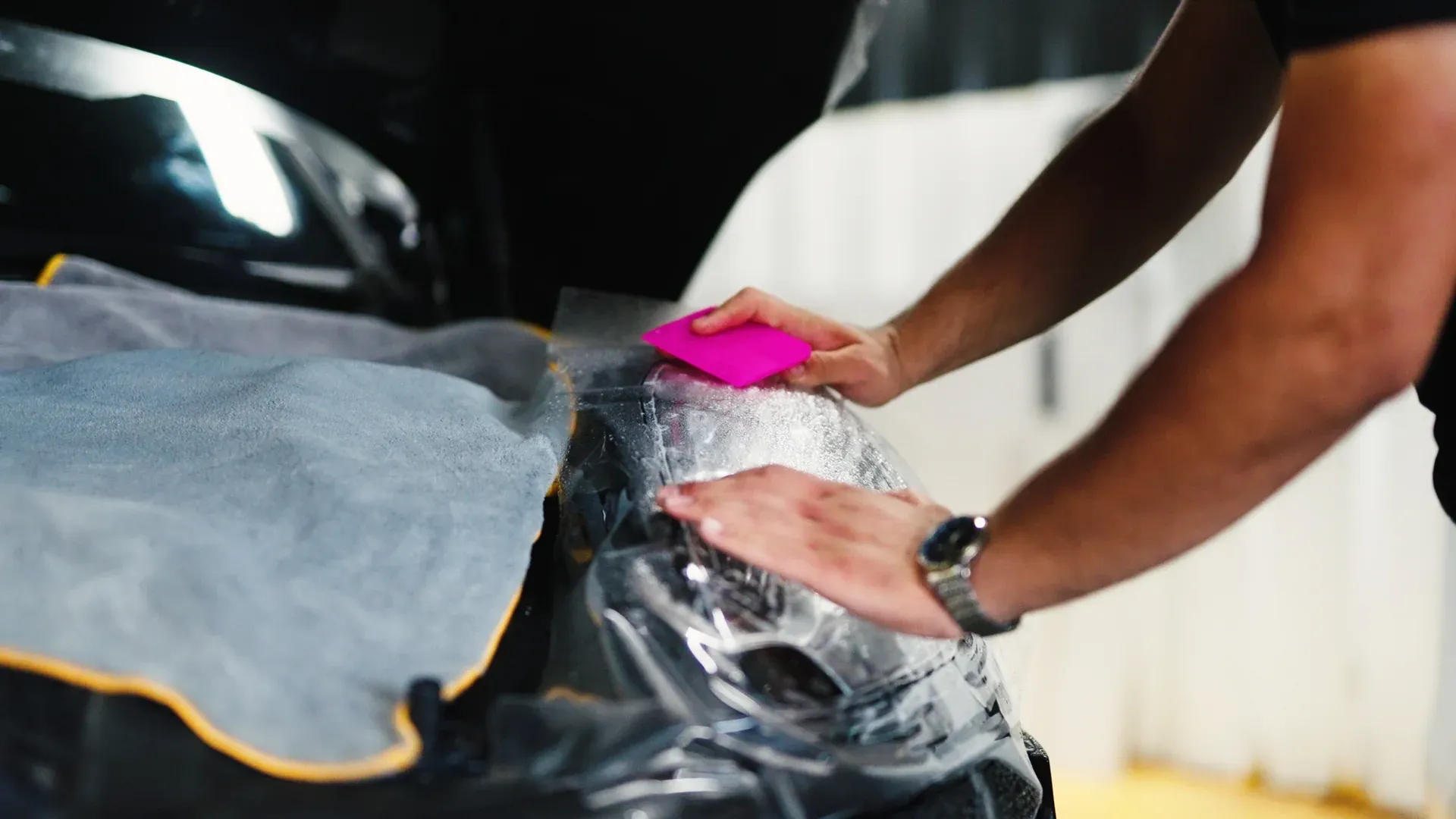 Technician squeegeeing paint protection film over a vehicle headlight.