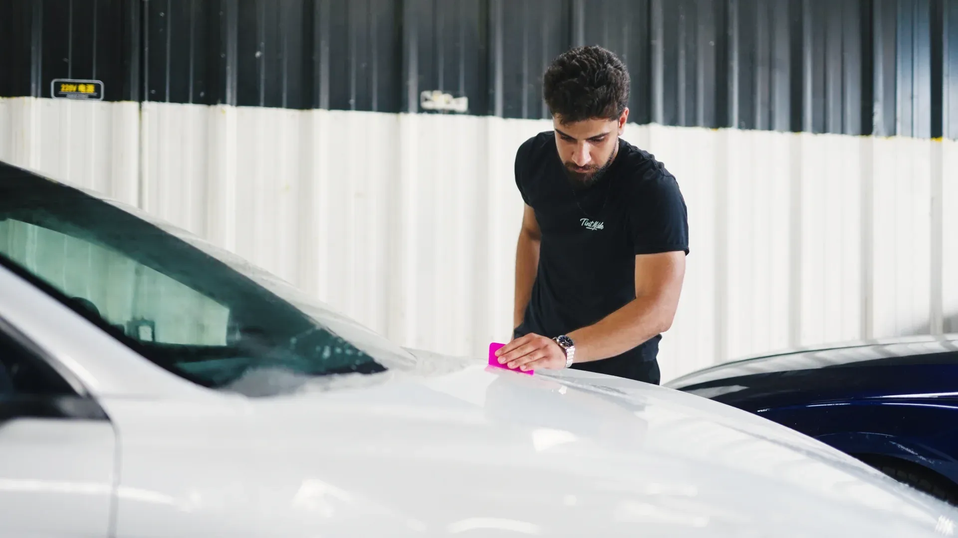 Technician smoothing paint protection film across a white vehicle hood.