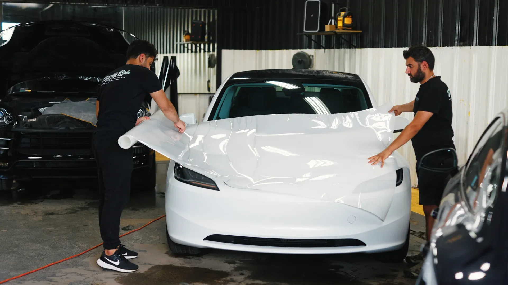 Two technicians positioning paint protection film across a white vehicle hood.