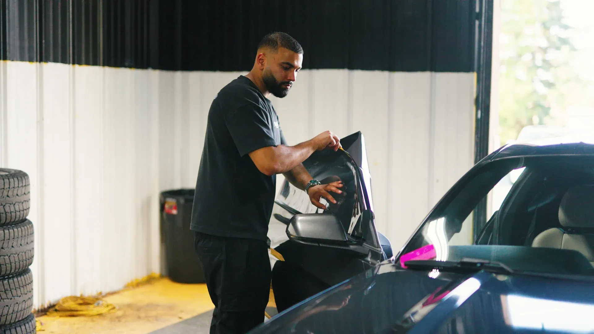 Technician installing window tint film at a vehicle door.