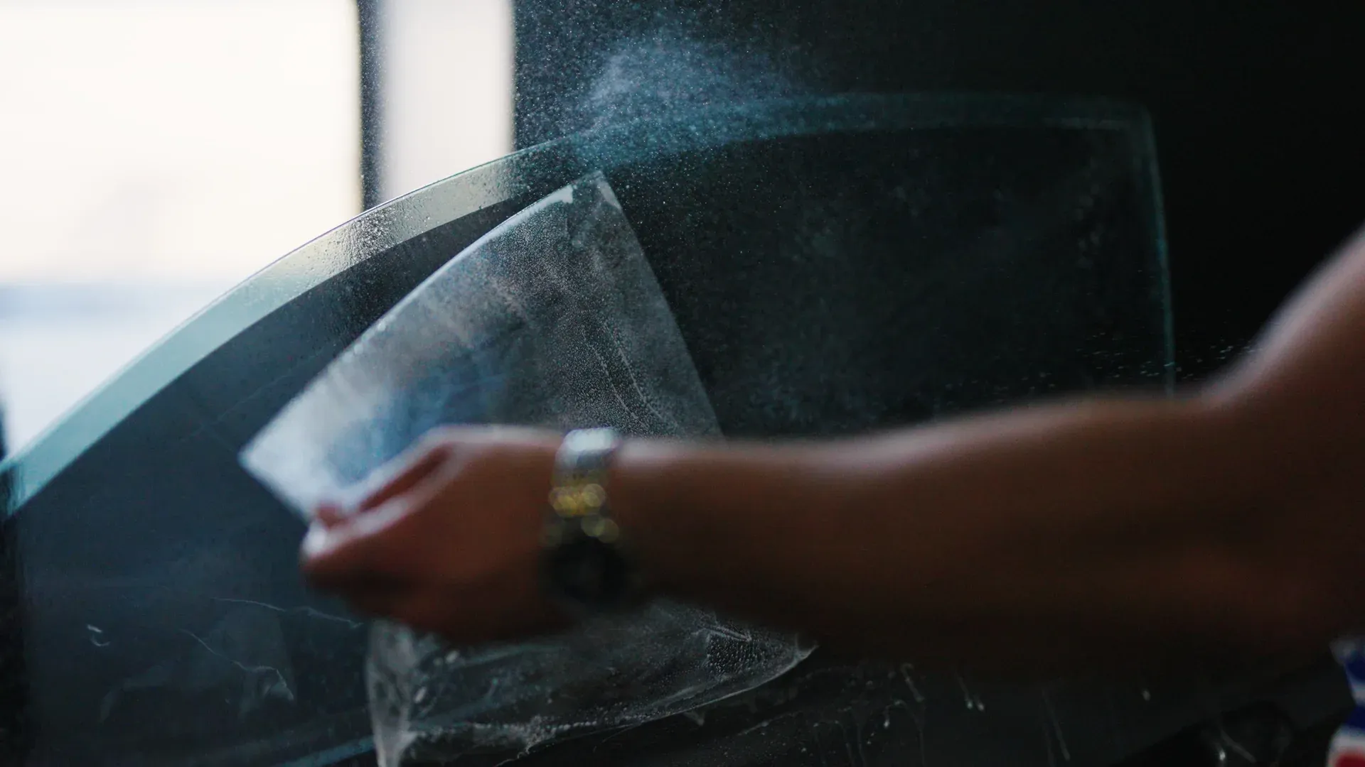 Window tint film sheets being sprayed before installation.